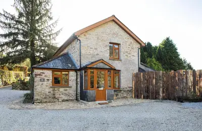 a small stone house with a wooden fence at Foxglove Cottage in Liskeard
