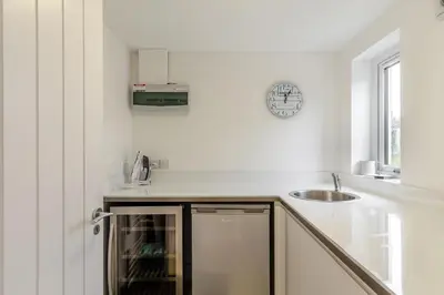 a white kitchen with a sink and a clock on the wall at 4 Bed in Widemouth Bay oc-s34119 in Widemouth Bay
