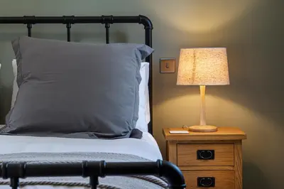 a bed with a lamp on a wooden night stand at Lowenna at Cusgarne Manor, rural, accessible in Cusgarne