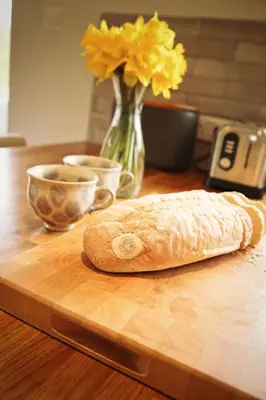 a loaf of bread on a cutting board with a vase of flowers at Little Croft- Walking paradise close to St Ives in St Ives