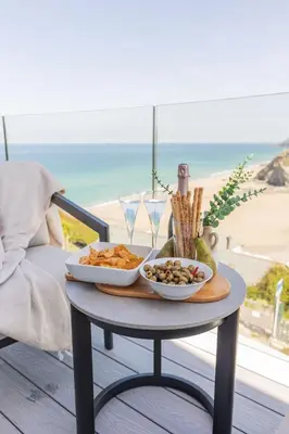 a table with two plates of food on a table with the beach at Ocean Skies in Porthtowan
