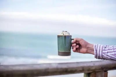 a hand holding a cup of coffee on a fence at Oceans Edge in Portreath