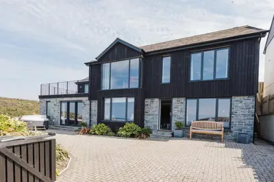 a black house with glass windows and a bench at Tamarisk in Portreath