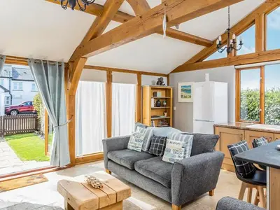 a living room with a gray couch and a kitchen at The Old Smithy in Bude