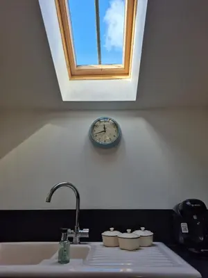 a clock on the wall above a sink under a window at The Granary -Trewen in Trewen