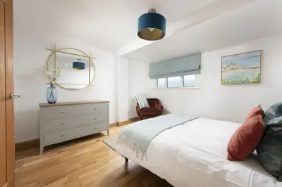 a bedroom with a bed and a dresser and a chair at Ocean View, Mawgan Porth - Sea Views - Hot Tub - Free Parking & WiFi in Mawgan Porth