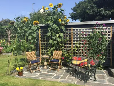 three chairs and a bench in a garden with sunflowers at The White Cottage B&B in Saint Teath