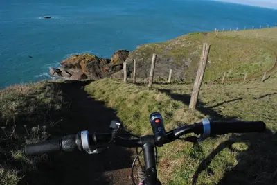 a picture of the handlebars of a bike on a path near the ocean at The White Cottage B&B in Saint Teath