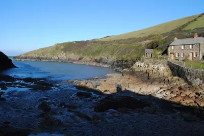 a house on a cliff next to a body of water at The White Cottage B&B in Saint Teath