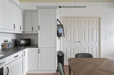 a kitchen with white cabinets and a door and a table at Apartment Sea Views & Parking Walk to Fistral in Newquay