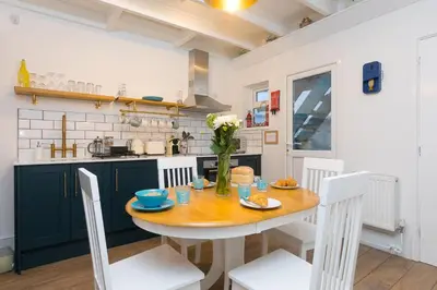 a kitchen with a wooden table and white chairs at Dan's Den in St Ives