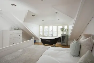a attic bedroom with a bed and a bath tub at Happy Days Cottage - Free WiFi - Minutes from Harbour & Beaches - Pets Welcome in St Ives