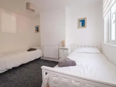 a white bedroom with two beds and a window at Trevarthian in St Austell