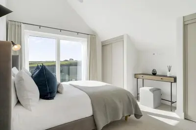 a white bedroom with a bed and a window at Modern Home with Stunning Gannel Estuary Views in Newquay