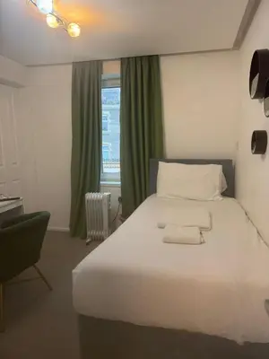 a bedroom with a white bed with a chair and a window at Dancenter Tolcarne Beach hotel in Newquay