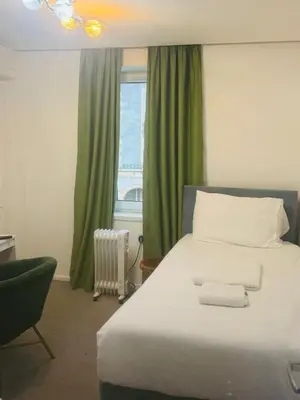a bedroom with a large bed with green curtains and a window at Dancenter Tolcarne Beach hotel in Newquay