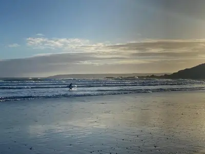 a person walking into the ocean with a surfboard at The Hexagon House in Penzance