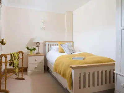 a white bedroom with a bed with a yellow blanket at The Granary, Engollan in Wadebridge