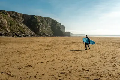 a man standing on a beach holding a surfboard at Stunning sea-view apartment close to Fistral Beach in Crantock
