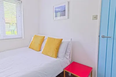 a white bed with yellow pillows and a red table at The Artist's Cottage in Uny Lelant
