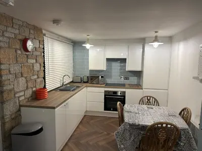 a kitchen with white cabinets and a table and a dining room at The Artist's Cottage in Uny Lelant