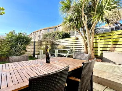 a wooden table with chairs and a bottle of wine at 3-Bedroom Holiday Home, Newquay with Garden & Parking - 150 Steps to the Beach! in Newquay