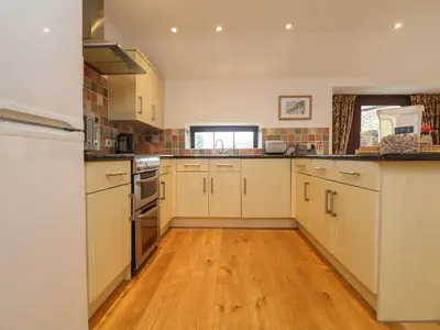 a kitchen with white cabinets and a wooden floor at Little Tregarrick in Helston