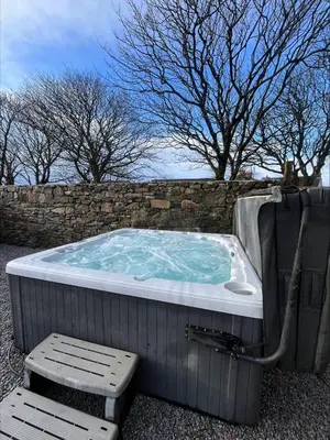a jacuzzi tub sitting next to a stone wall at Cosy Cottage Hot Tub Sleeps 8 Log Fires in Carnbrea