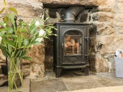 a stove in a stone wall with a vase of flowers at Driftwood Cottage in Helston