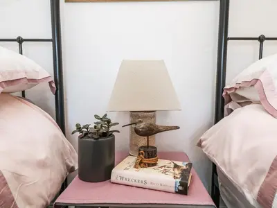 a lamp on a bedside table with a book at Driftwood Cottage in Helston