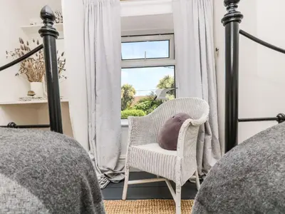 a bedroom with a bed and a chair and a window at Driftwood Cottage in Helston