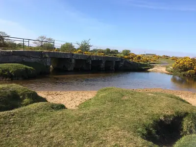 a bridge over a body of water with grass at Barn Cottage in Saint Breward