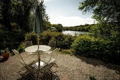a table and chairs with an umbrella and a river at Pencreek in Kea