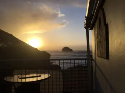 a sunset over the ocean with tables on a balcony at Praxis Trebarwith Strand in Treknow