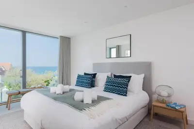 a white bedroom with a large bed with blue pillows at Beachfront Townhouse Lovely Sea Views Newquay in Newquay
