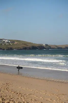 a person walking on the beach with a surfboard at Spacious House Sea Views Opposite Beach in Newquay