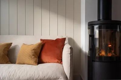 a fireplace sitting next to a white couch with pillows at Cosy Beach House on the Seafront Porthleven in Porthleven