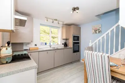 a kitchen with white cabinets and a wooden table at Rumsdale - Luxury Cottage in Looe