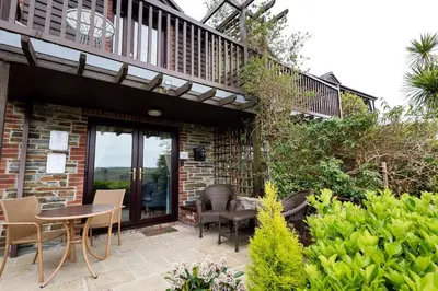 a patio with a table and chairs and a balcony at Rumsdale - Luxury Cottage in Looe
