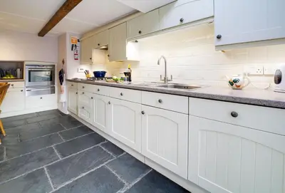 a kitchen with white cabinets and a tile floor at Hardys in Padstow