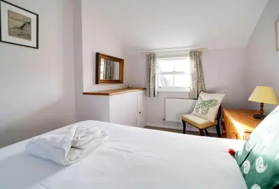 a bedroom with a white bed with a chair and a window at Hardys in Padstow