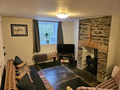 a living room with a stone fireplace and a television at Seahorse Cottage in Boscastle