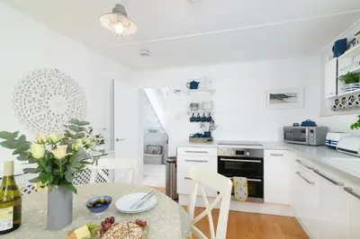 a white kitchen with a table and chairs at Sealight Cottage in St Ives