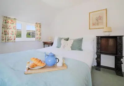 a bed with a tray of croissants and a tea pot and a plate at Rose Hill Cottage in Port Isaac
