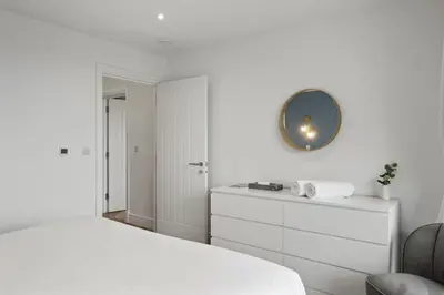 a white bedroom with a bed and a mirror on the wall at Modern Apartment Opposite Beach Parking & Balcony in Newquay