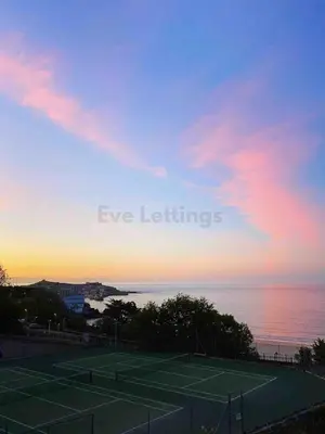 a tennis court in front of the ocean at sunset at Modern classic seaside apartment with parking and balcony in St Ives