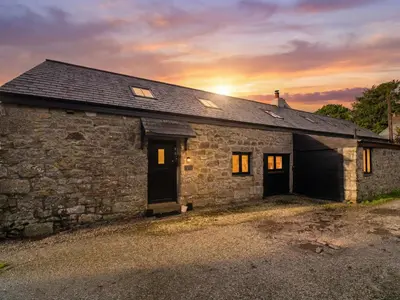 a stone house with the sun setting behind it at Riverside Barn in Truro
