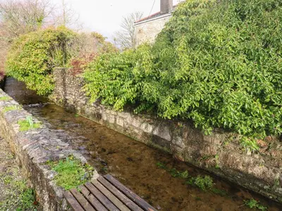 a river with a wooden bench next to a wall at Riverside Barn in Truro
