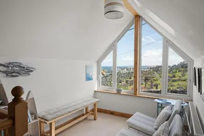an attic room with large windows and a bench at Spacious Home Overlooking Porthmeor Beach Parking in St Ives