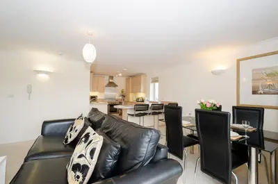 a living room with a black leather couch and a dining room at Russell Court 2 - Beautifully furnished modern apartment with parking and views over Looe river and town in Looe